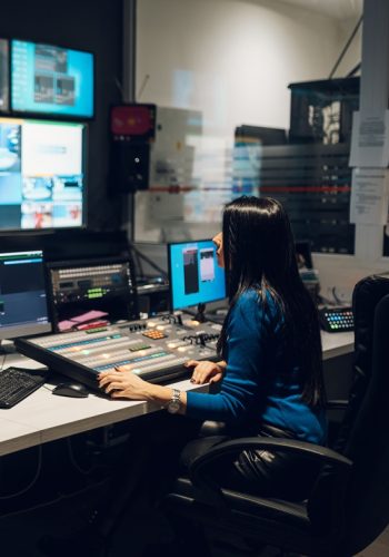 Middle aged woman using equipment in control room on a tv statio Beautiful middle aged beautiful woman working on a tv station as a producer in a broadcast control room. Show production maker. Television.